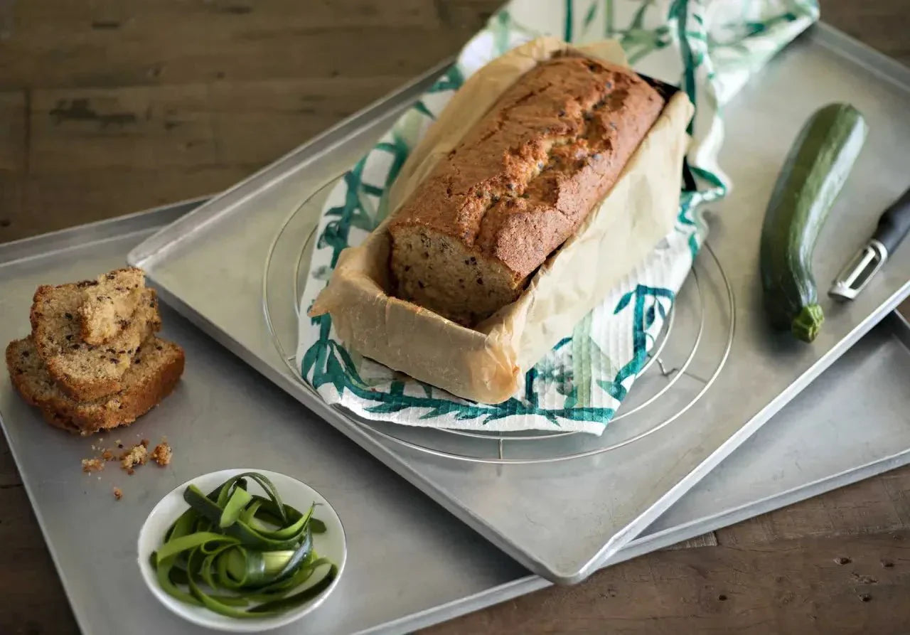 Zucchini-Kuchen in einer Brotform auf einem Blech mit Zucchinischeiben und einem frischen Zucchino daneben.