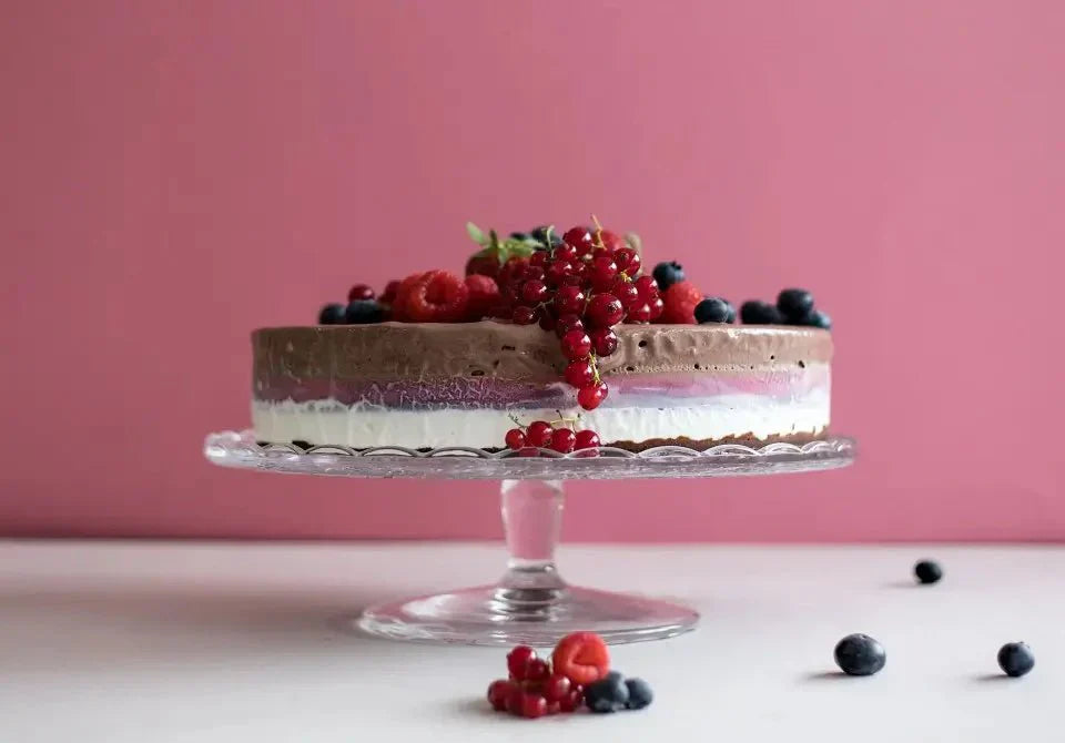 Schokoladen-Eistorte mit Beeren auf gläserner Tortenplatte vor rosa Hintergrund.