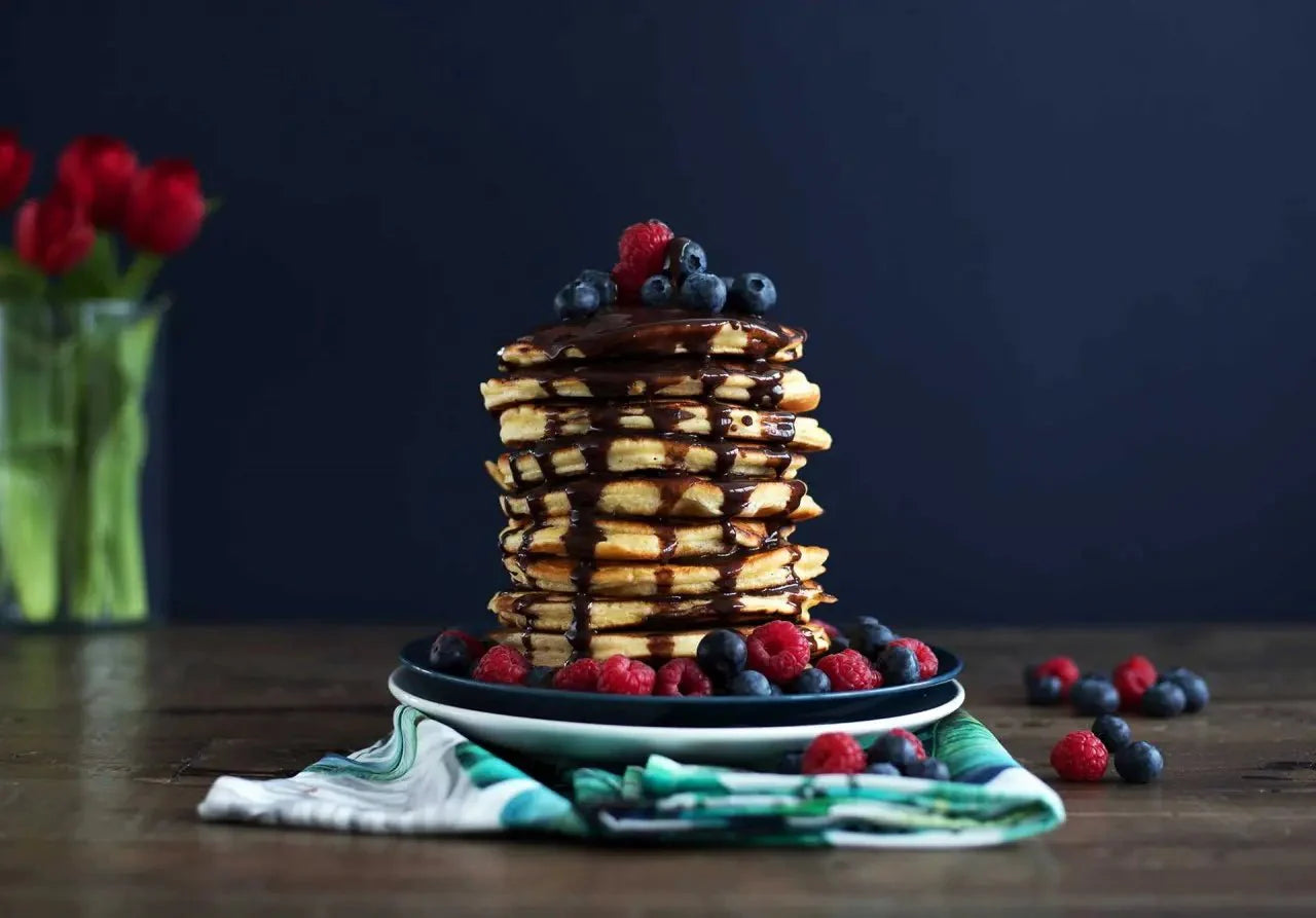 Stapel Fluffiger Pancakes mit Schokoladen-Ahornsirup und Beeren, serviert auf einem Teller mit dunklem Hintergrund.