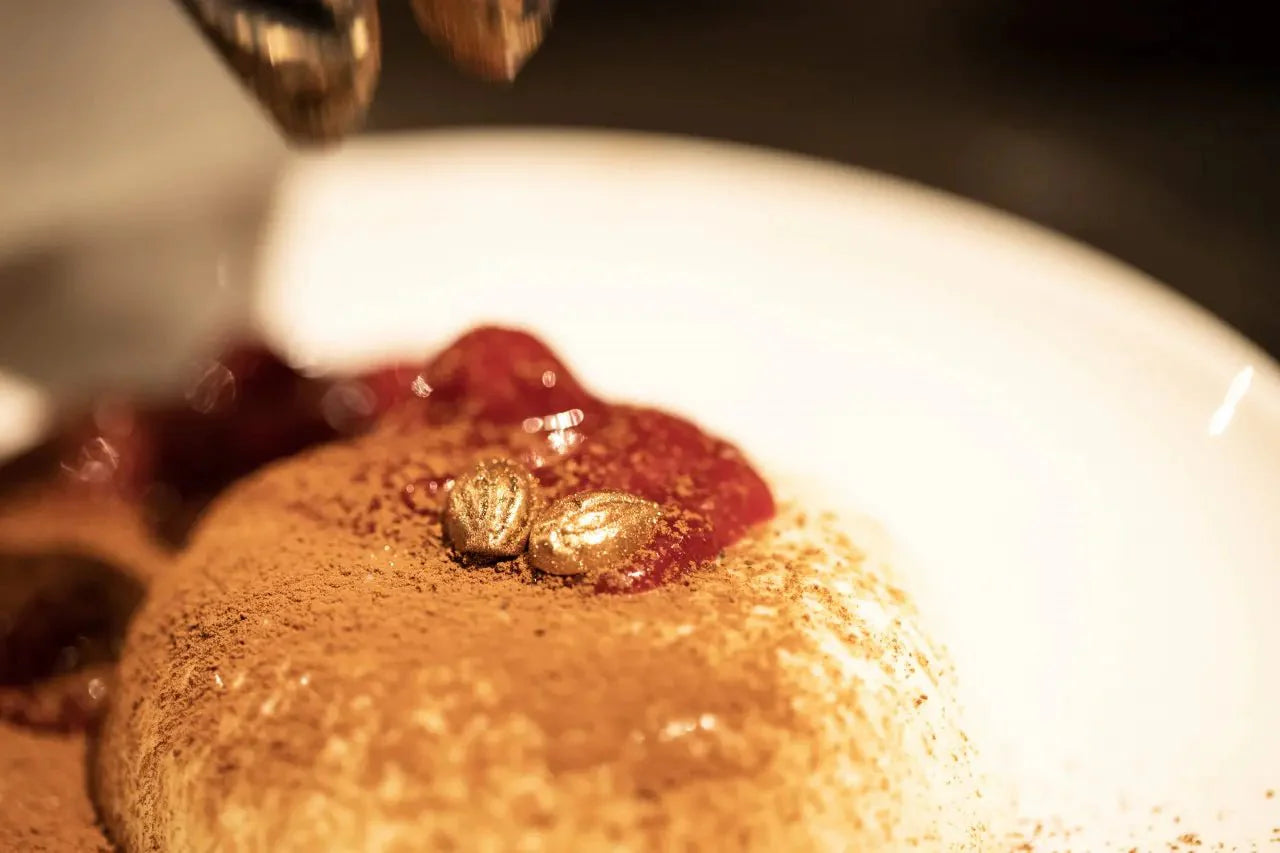 Nahaufnahme von Panna Cotta mit Eierlikör, bedeckt mit Kakaopulver und roten Fruchtsoßen auf einem weißen Teller.