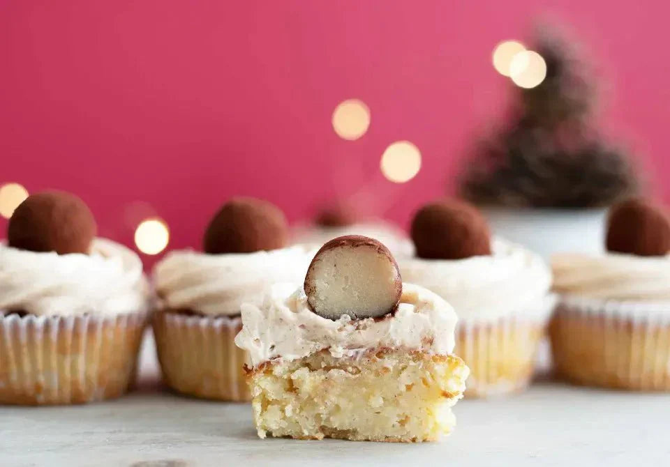 Apfel-Marzipan-Cupcakes mit Sahnehaube und Schokoladentrüffel, vor einem roten Hintergrund arrangiert.