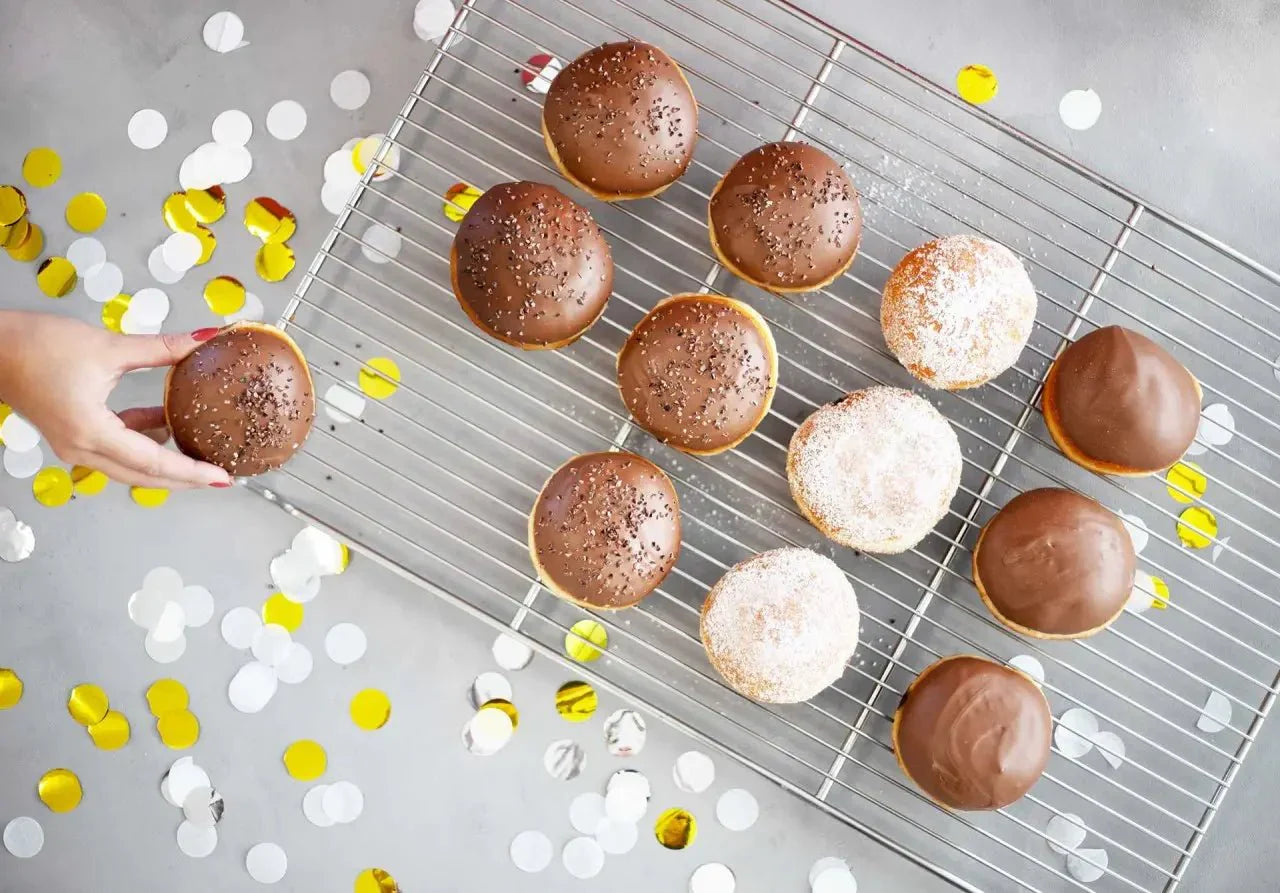 Berliner Pfannkuchen mit Nougatfüllung und Zucker, auf einem Gitterrost, umgeben von buntem Konfetti.