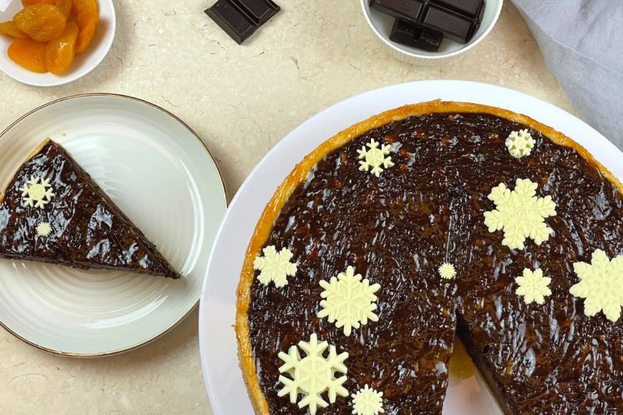 Schokoladenkuchen mit Schneeflockendekor und Aprikosen, dazu Schokoladenstückchen auf heller Marmoroberfläche.