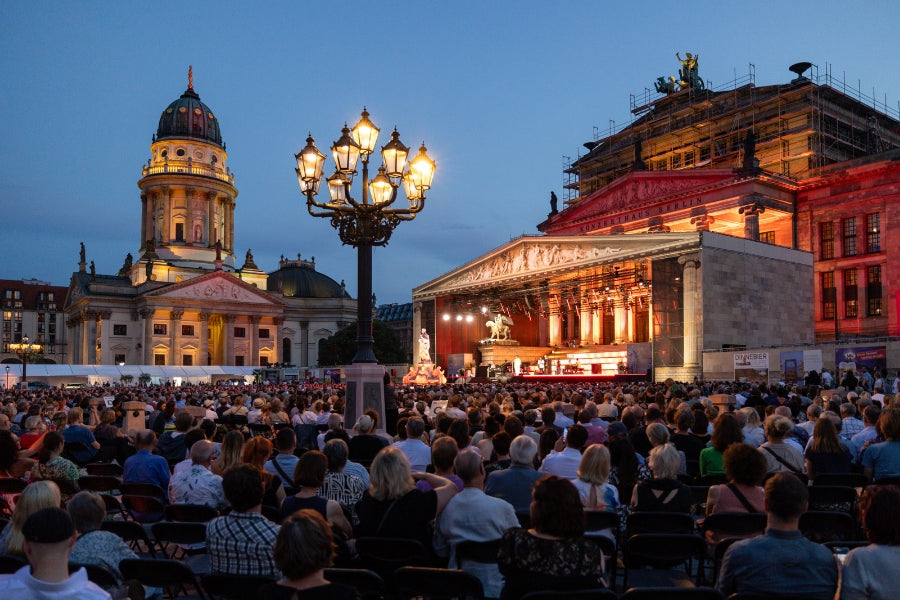 Open-Air-Konzert in Berlin bei Abenddämmerung, Menschen auf Stühlen vor beleuchteten historischen Gebäuden.