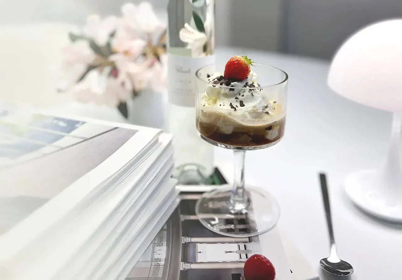 Elegantes Tiramisu im Glas mit Kakaolikör, Sahne, Schokolade und Erdbeeren, dekoriert neben Blumen und Büchern.