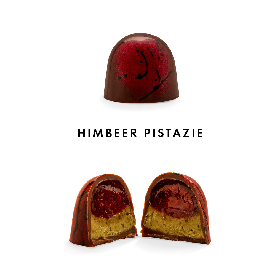 Handwerkliche Praline Himbeer Pistazie mit roter Schokolade und Maserung, halbe Praline offen. - Rausch