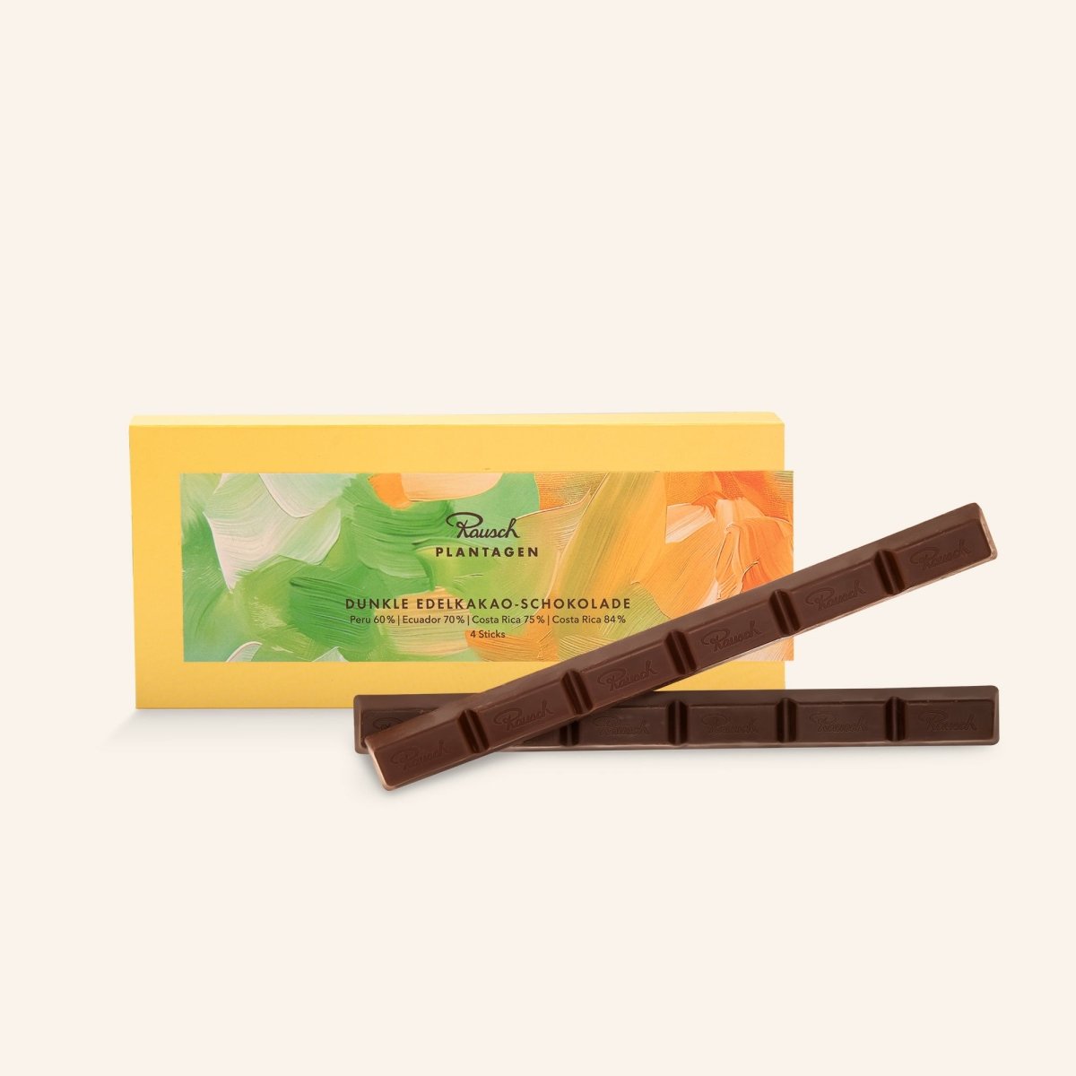 Gelbe Verpackung mit fröhlichen grün-orangen Pinselstrich-Mustern. Im Vordergrund zwei Rausch Plantagen Sticks aus dunkler Edelkakao-Schokolade.