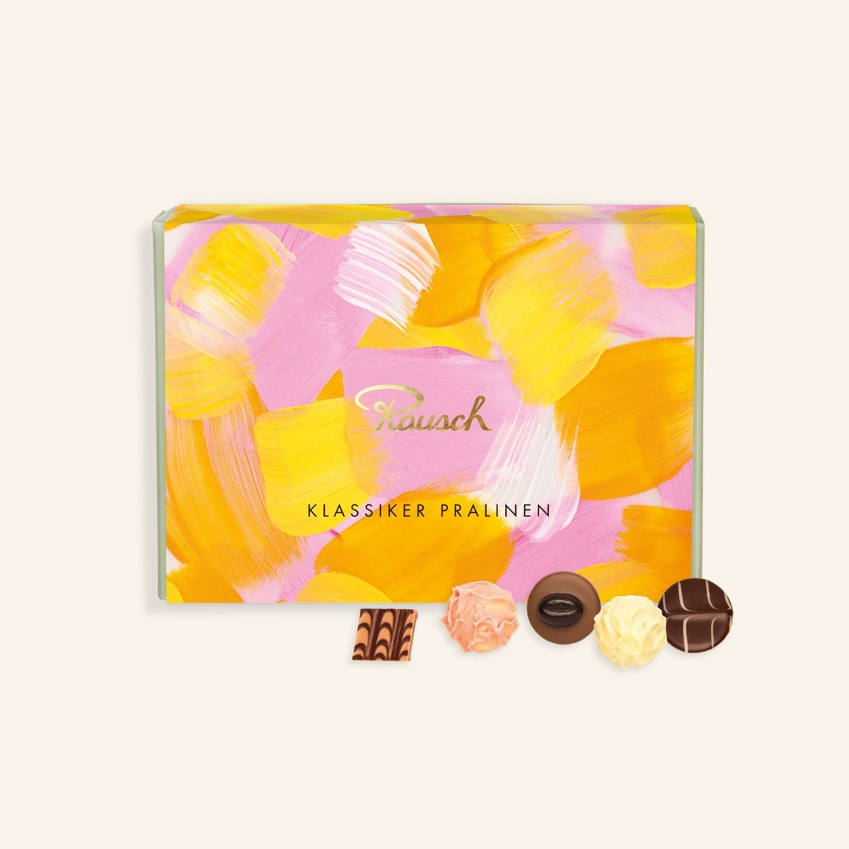 Rosa-orange Pralinenschachtel mit Pinselstrich-Muster. Vor der Schachtel liegen fünf verschiedene Pralinen.
