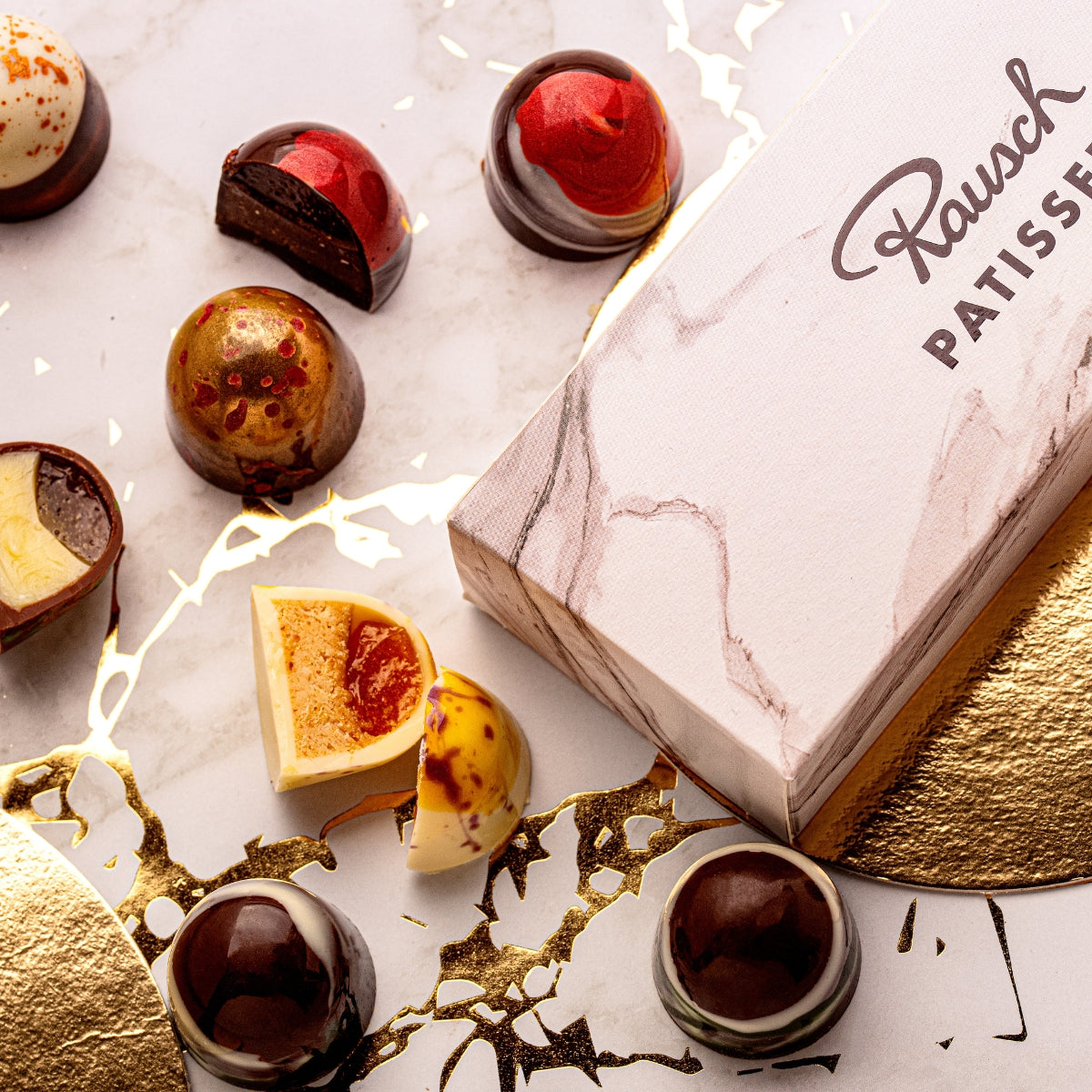 Handwerkliche Pralinen in rot und braun mit glänzender Schokoladenhülle, edle Geschenkbox. - Rausch