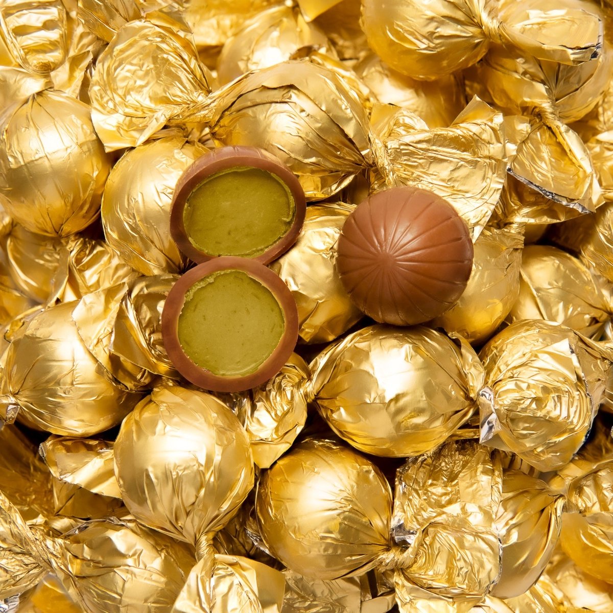 Viele goldene Pralinenkugeln. Auf den goldenen Kugeln liegt eine ganze und eine halbierte Dubai-Pralinenkugel.